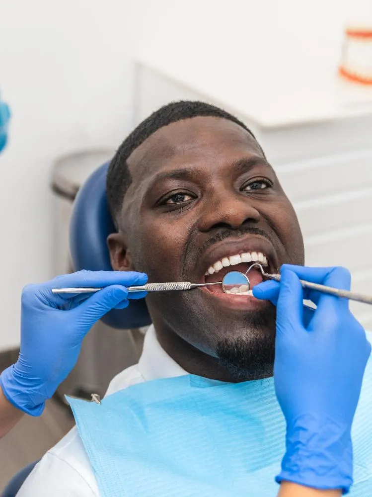 Dental Hygienist Examining An African Male Patient